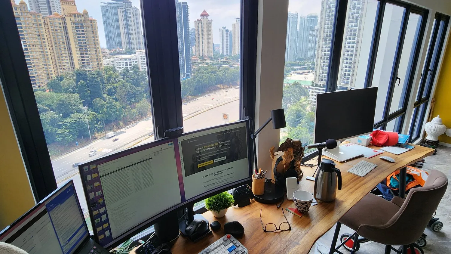 A corner room in Kuala Lumpur, a long live-edge desk running under floor-to-ceiling windows with the city outside